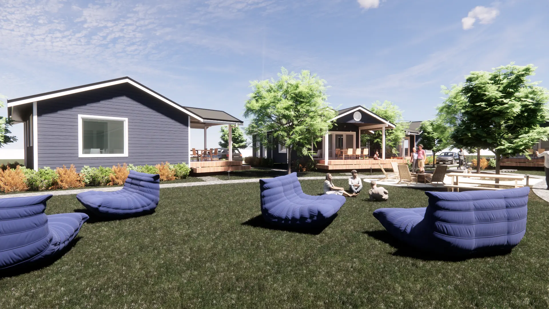 Summer communal yard with blue modern cottages, large green trees, wooden decks, lounge chairs, and groups of people relaxing on a grassy lawn.